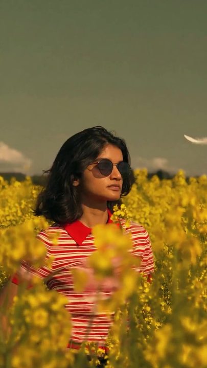 Mulher de óculos escuros e camiseta listrada num campo de flores amarelas