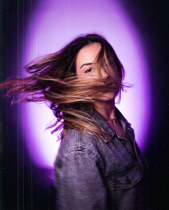 Mulher girando o rosto com o cabelo em movimento e rastro de exposição longa, sob luz roxa
