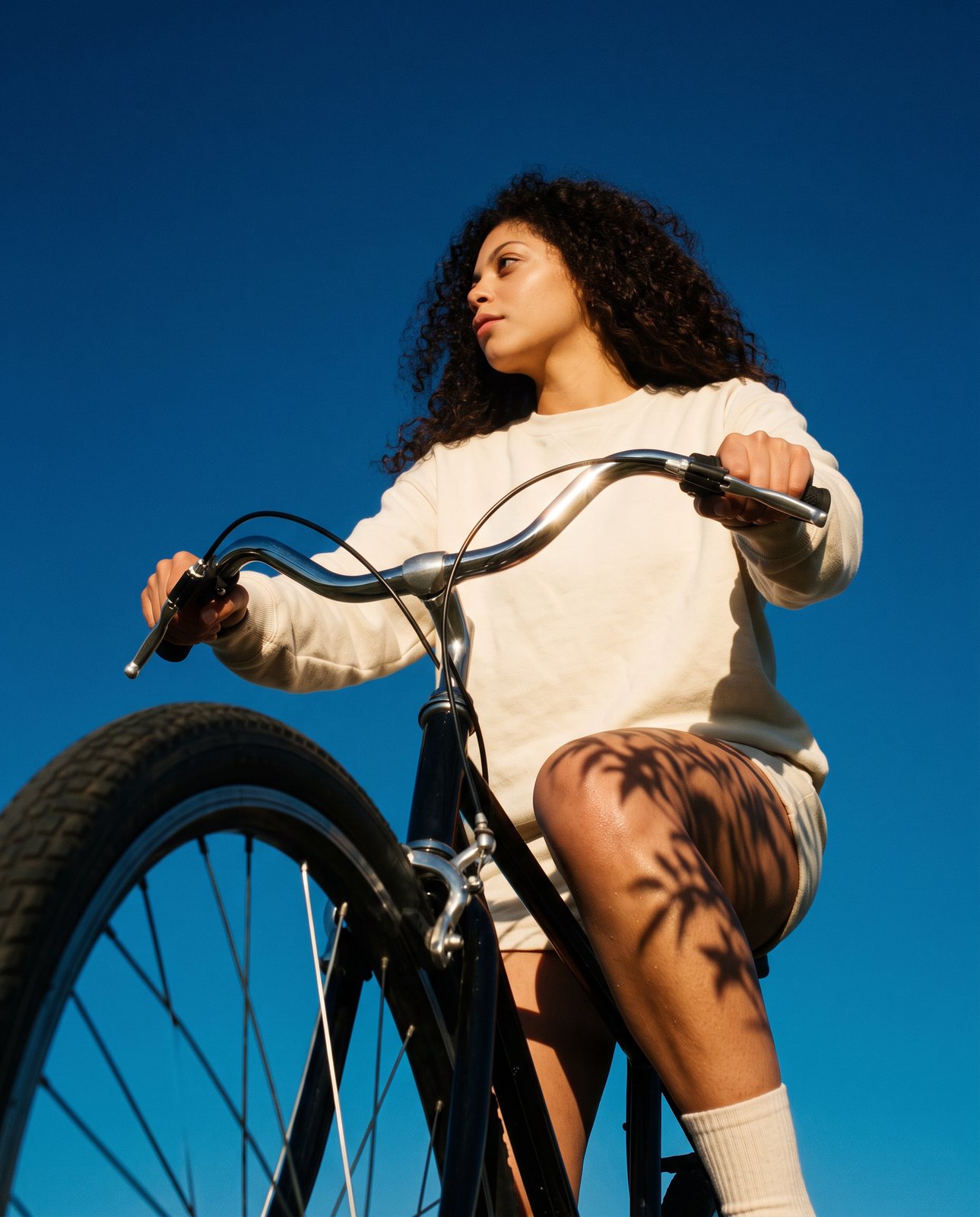 Modelo de cabelo cacheado numa bicicleta, vista de baixo contra o céu azul