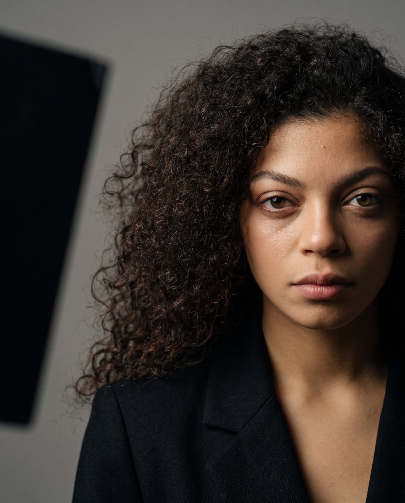 A mesma modelo gerada em estúdio, de blazer preto contra fundo cinza, com luz lateral